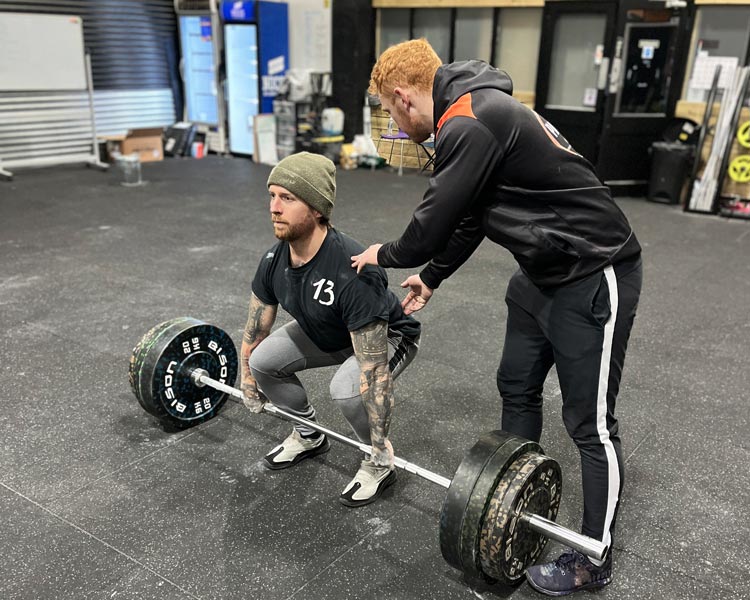 personal coach adjusting his trainee position for weight lifting